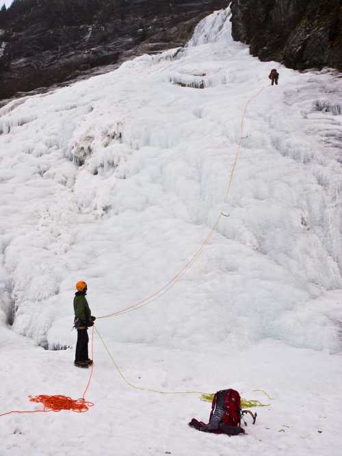 Two climbers ascend an icy slope, one at the top and one at the bottom, with climbing gear and ropes visible.