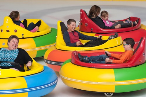 A group of children and adults enjoy bumper cars on ice, laughing and having fun in colorful, inflatable vehicles.