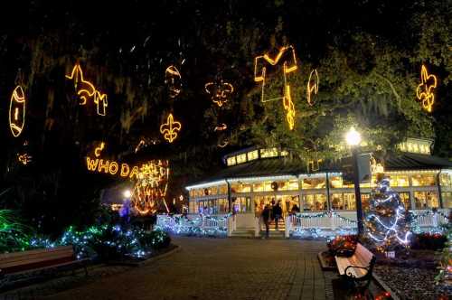 A festive scene with holiday lights, including sports symbols, a Christmas tree, and a decorated gazebo at night.