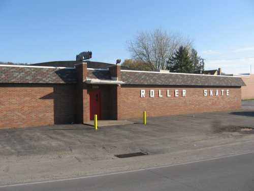 A brick building with a sign reading "ROLLER SKATE" and a red door, set against a clear sky and trees.