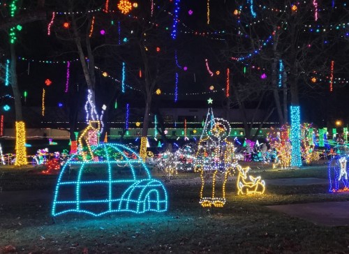Colorful holiday lights illuminate a park scene with an igloo, a figure, and various festive decorations.