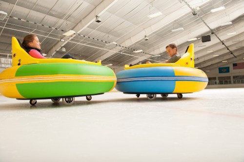 Two children sit in colorful inflatable bumper cars on an ice rink, enjoying a fun activity.