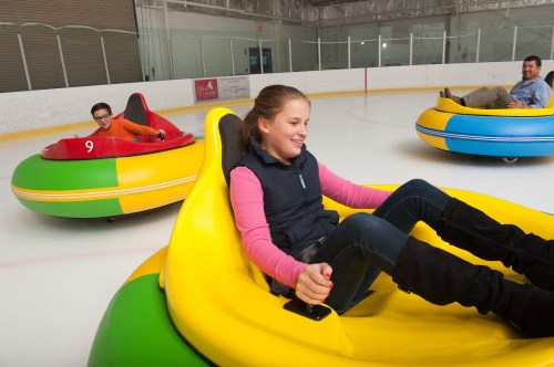 Three people enjoy bumper cars on ice, smiling and having fun in colorful, inflatable vehicles.
