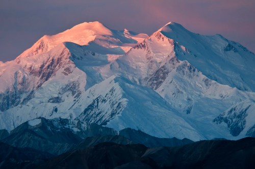 Snow-capped mountains bathed in soft pink light during sunset, showcasing rugged peaks and glistening glaciers.