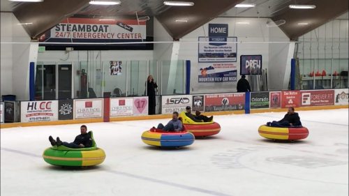 Four people sit in colorful inflatable tubes on an ice rink, enjoying a fun activity.