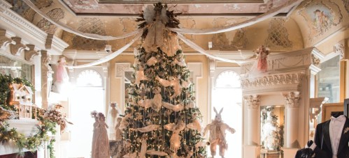 A beautifully decorated Christmas tree in an elegant room, adorned with ribbons and surrounded by festive decor.