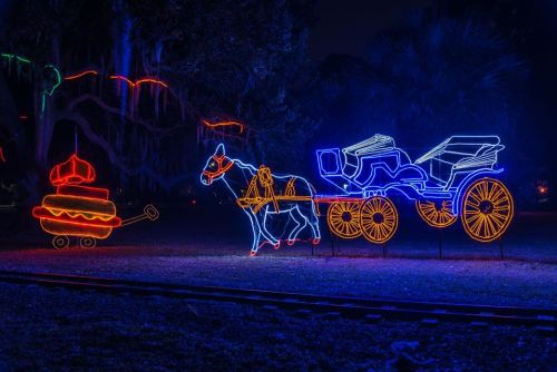 Neon light display featuring a horse-drawn carriage and a colorful carousel in a nighttime setting.