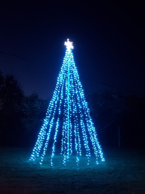 A tall Christmas tree made of blue lights, glowing brightly against a dark night sky.