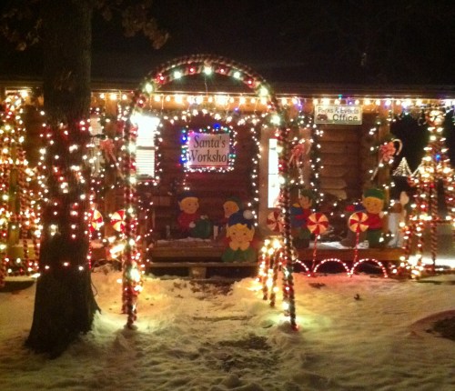 A festive cabin decorated with colorful lights and candy cane motifs, labeled "Santa's Workshop," surrounded by snow.