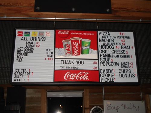 Menu board displaying drinks, pizza, nachos, hotdogs, and snacks with prices and a "Thank You" message.
