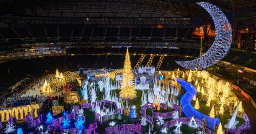 A brightly lit holiday display in a stadium, featuring a large tree, colorful lights, and festive decorations.