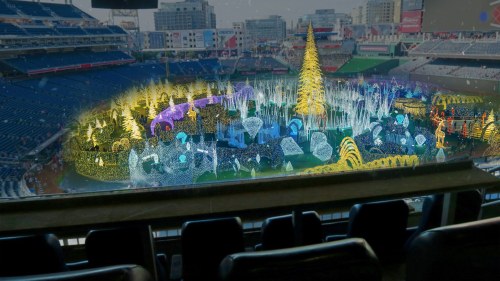 A colorful holiday light display featuring a large tree, set in a stadium with empty seats in the foreground.