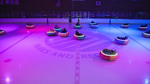 Colorful bumper cars on an ice rink, illuminated by vibrant lights, with a "Parks and Recreation" logo in the center.