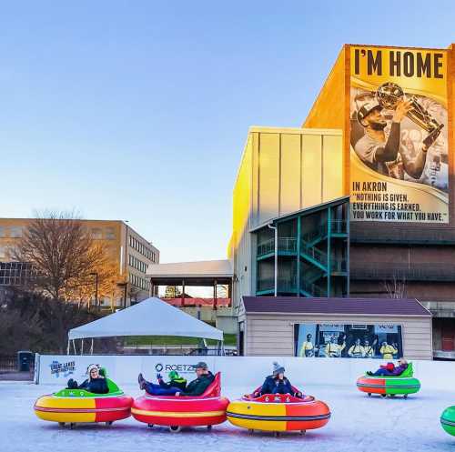 People sitting in colorful inflatable tubes on an ice rink, with a large sign reading "I'M HOME" in the background.