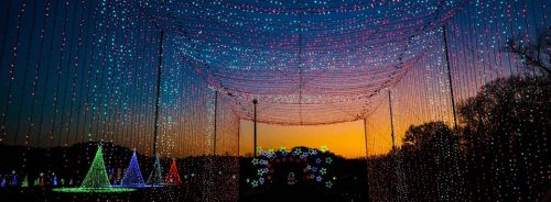 A vibrant display of colorful lights hangs above a landscape at sunset, creating a festive atmosphere.