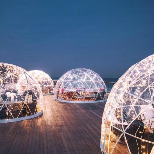A scenic view of illuminated igloo-like structures on a wooden deck, set against a twilight sky.
