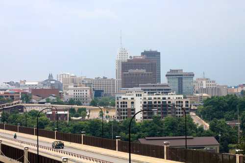 City skyline featuring modern buildings and a highway in the foreground, under a cloudy sky.