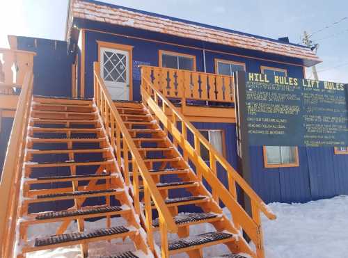 A colorful building with orange stairs and a sign displaying hill rules, surrounded by snow.