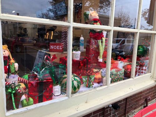 A festive window display featuring holiday decorations, toys, and lights in red and green colors.