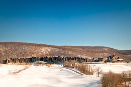 A snowy landscape featuring a large resort building against a backdrop of hills and a clear blue sky.