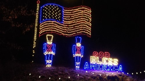 A festive display featuring a lit American flag and two toy soldiers with the words "God Bless America."