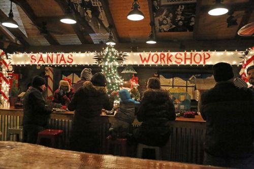 A festive workshop scene with people gathered around a counter, decorated with lights and a Christmas tree.