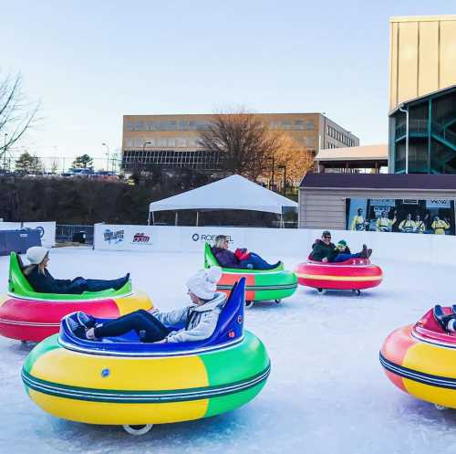 A group of people enjoying ice tubing on a frozen surface, surrounded by buildings and a clear blue sky.