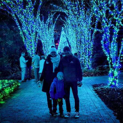 A family stands together under glowing blue and white holiday lights in a festive outdoor setting.