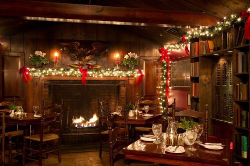 Cozy restaurant interior with a fireplace, festive decorations, and tables set for dining. Warm, inviting atmosphere.