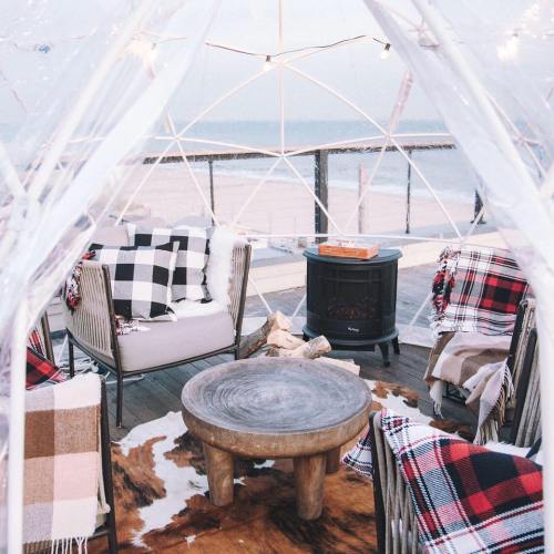 Cozy outdoor seating area with blankets, a wooden table, and a small heater, overlooking the beach.