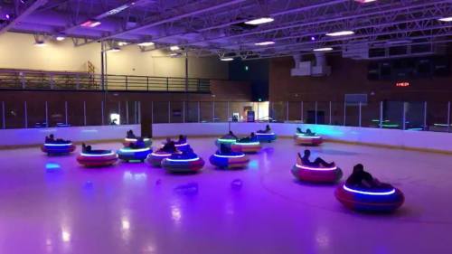A brightly lit ice rink with colorful bumper cars and people enjoying a fun activity.