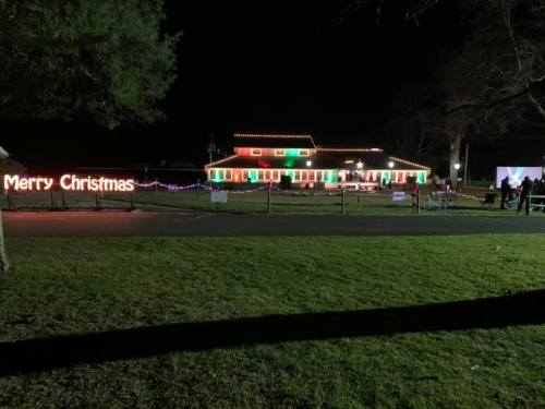 A brightly lit house decorated for Christmas at night, with colorful lights and a "Merry Christmas" sign in the yard.