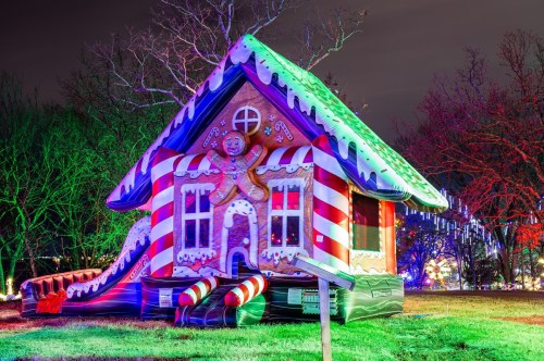 A colorful inflatable gingerbread house with candy decorations, illuminated at night in a festive outdoor setting.
