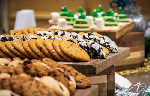 A variety of cookies displayed on wooden platters, including chocolate chip and festive holiday shapes.