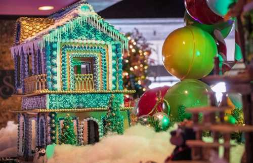A colorful gingerbread house decorated with icing and candy, surrounded by festive balloons and holiday decorations.