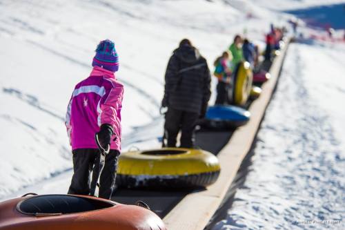Children and adults walking on a snowy path, pulling colorful snow tubes behind them.