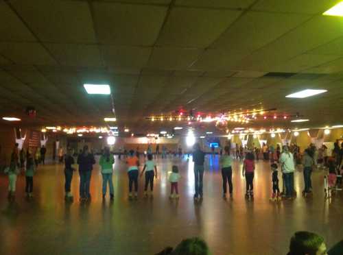 A group of people skating in a brightly lit roller rink with colorful lights and a disco ball.