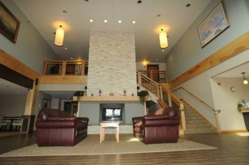 A spacious lobby with two leather sofas, a stone fireplace, and a staircase, featuring warm lighting and wooden accents.