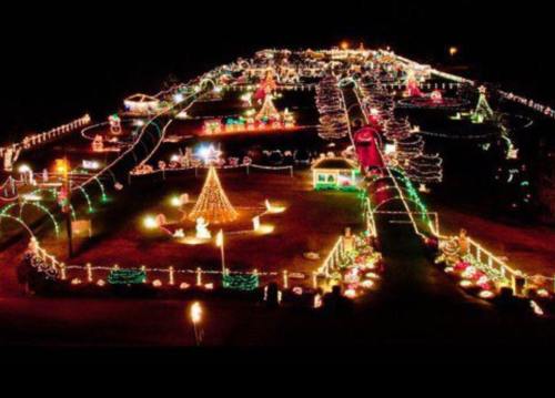 Aerial view of a festive holiday display with colorful lights, decorated trees, and festive figures in a large outdoor area.