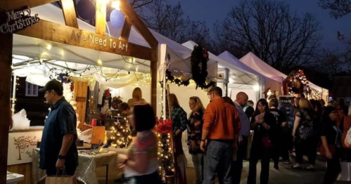 A festive market scene with people browsing art and crafts under illuminated tents during the holiday season.