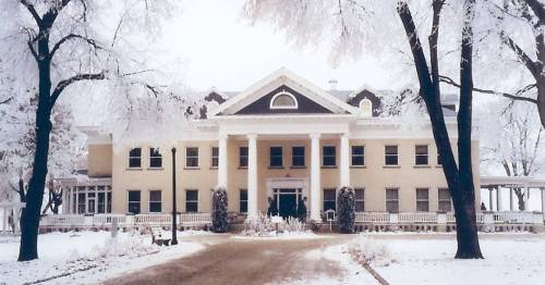 A large, historic building surrounded by snow-covered trees and a frosty landscape.