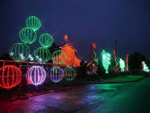 Colorful holiday lights in various shapes illuminate a dark street, creating a festive atmosphere.