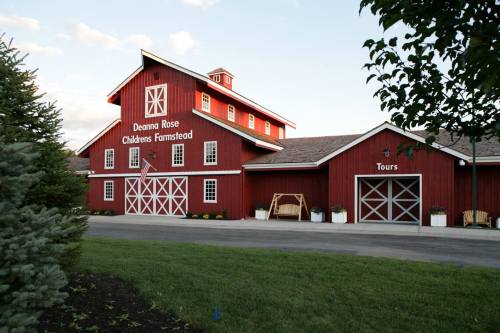 Red barn building with "Deanna Rose Children's Farmstead" sign, surrounded by greenery and a clear blue sky.