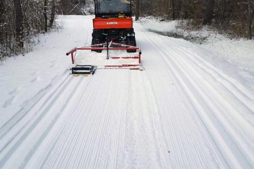 A snow grooming machine on a snowy trail, creating smooth, groomed tracks in the fresh snow.