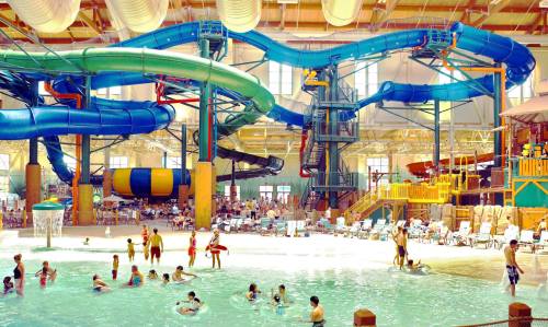 Indoor water park featuring colorful slides, a wave pool, and families enjoying the water and sun.