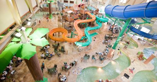 Aerial view of a vibrant indoor water park with slides, pools, and seating areas filled with families enjoying the space.