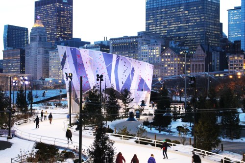 People ice skating in a city park with modern architecture and skyscrapers in the background during twilight.