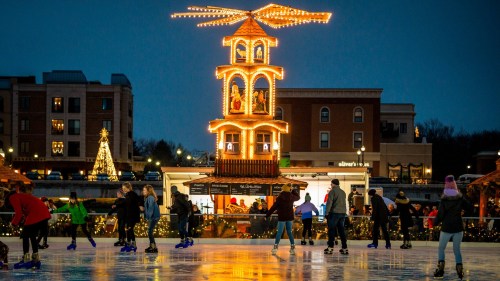 Skaters enjoy an outdoor ice rink at dusk, featuring a lit holiday carousel and festive decorations in the background.