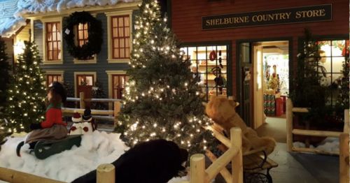 A festive display featuring a decorated Christmas tree, snow, and holiday decorations outside a country store.