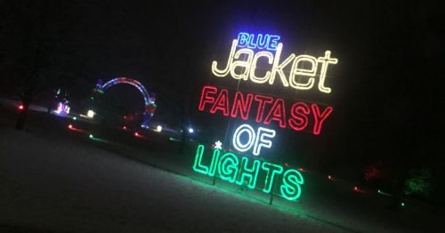 Colorful neon sign reading "Blue Jacket Fantasy of Lights" in a snowy park at night.